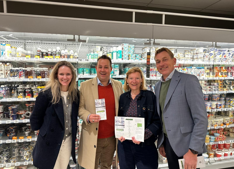 Vier betrokkenen van het CBL houden de samenwerkingsovereenkomst vast in een supermarktomgeving 