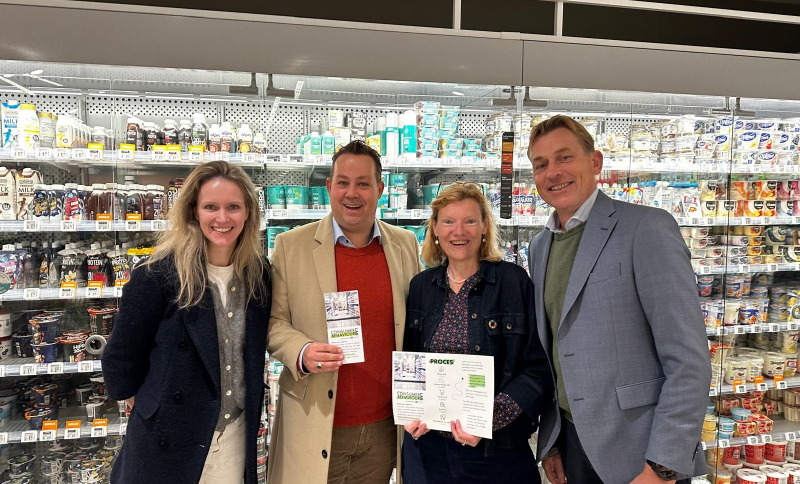 Vier betrokkenen van het CBL houden de samenwerkingsovereenkomst vast in een supermarktomgeving 
