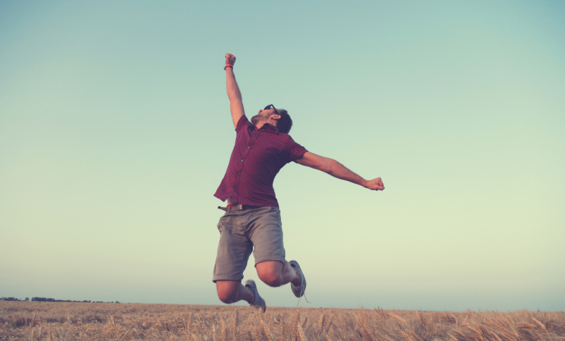 Een jonge man springt juichend omhoog in de buitenlucht als symbool voor een energieke start van ondernemerschapsambities.