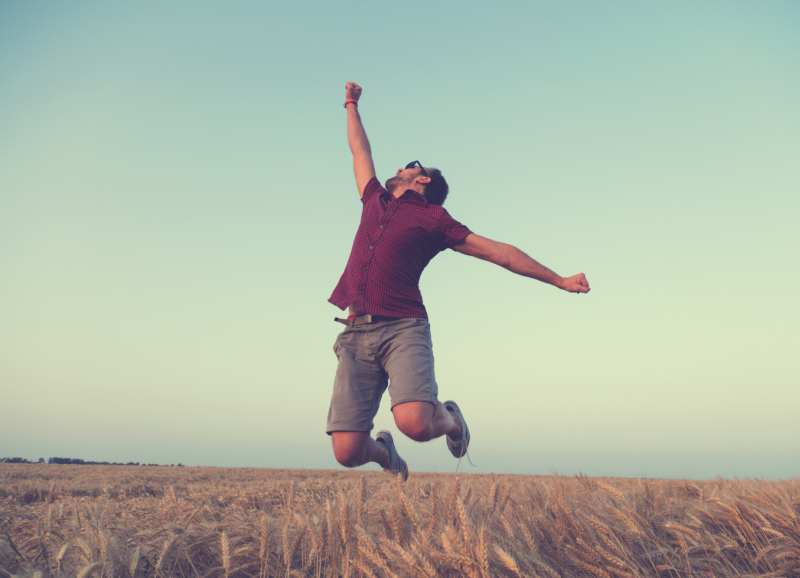 Een jonge man springt juichend omhoog in de buitenlucht als symbool voor een energieke start van ondernemerschapsambities.