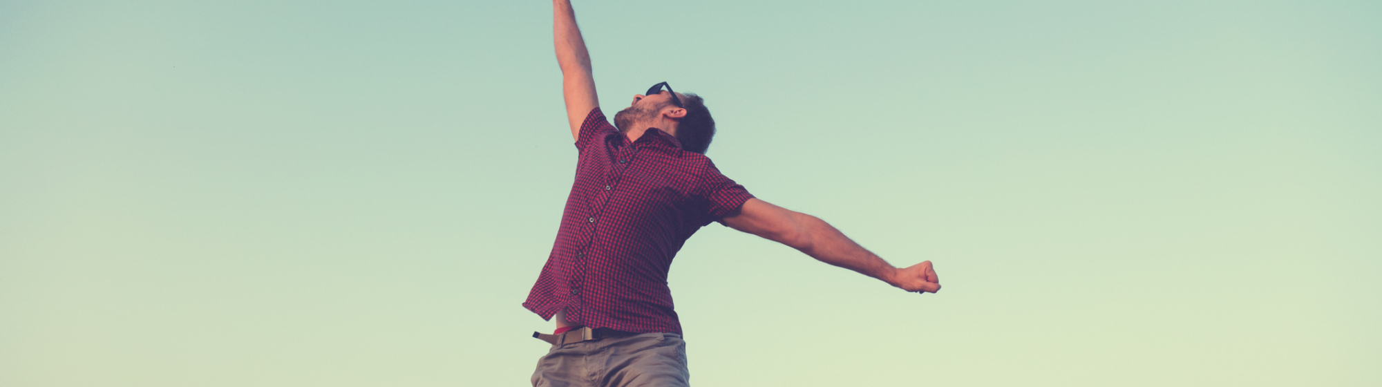 Een jonge man springt juichend omhoog in de buitenlucht als symbool voor een energieke start van ondernemerschapsambities.