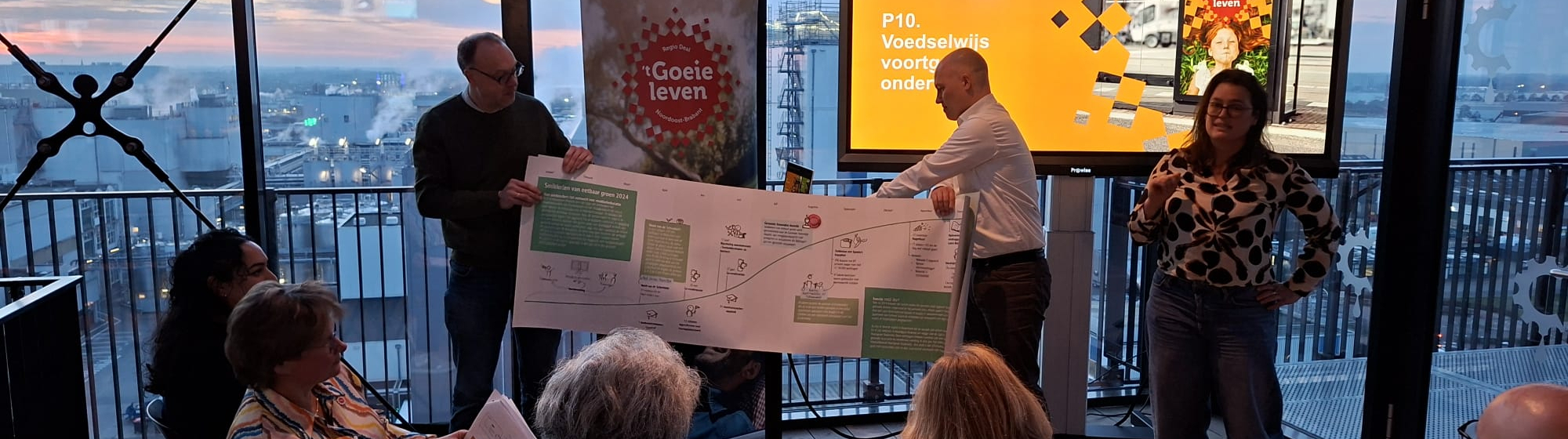 Presentatie van een Regio Deal‑programma waarbij deelnemers een visual tonen tijdens een bijeenkomst in The Chocolate Factory met uitzicht over de stad.